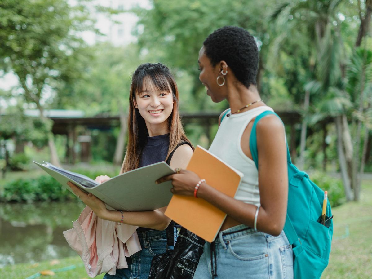 Two students talking together outdoors, one listening closely.